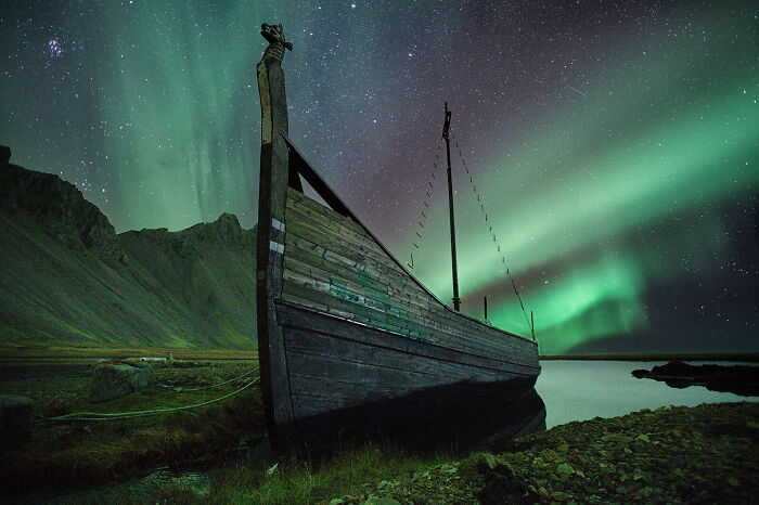 Wooden boat under vibrant northern lights and starry sky, showcasing a completely different perspective of our world.