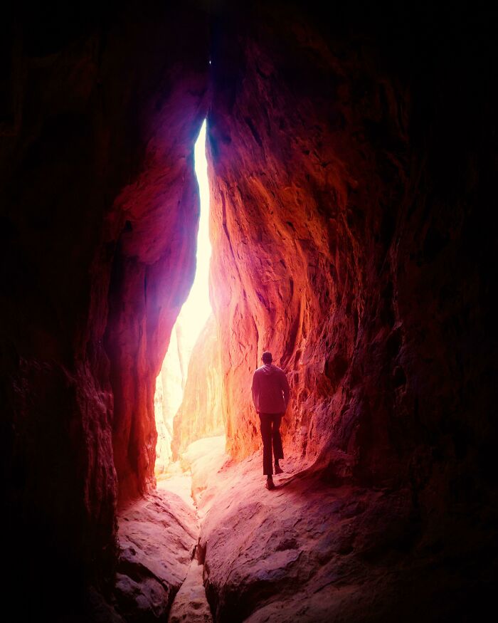 Person walking through a narrow red rock formation illuminated by sunlight in amazing pics showing our world perspective.