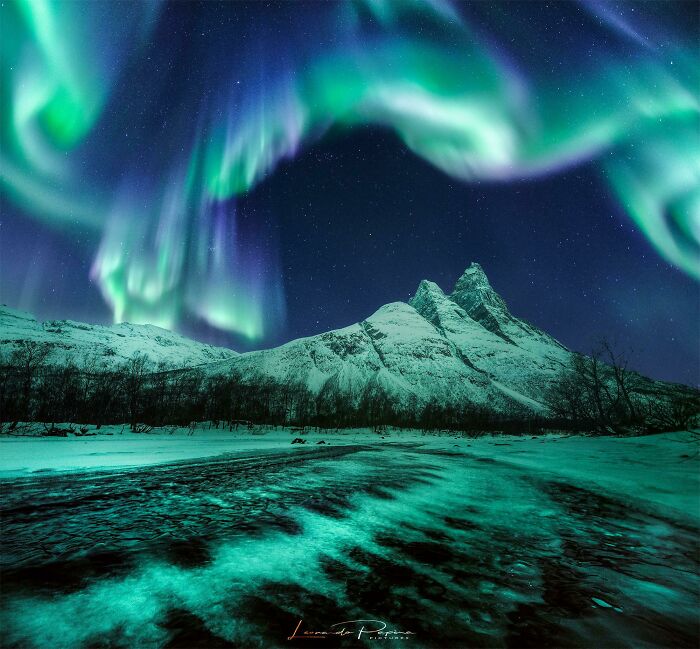 Aurora borealis glowing over snow-covered mountains and a frozen landscape, showcasing a unique world perspective.