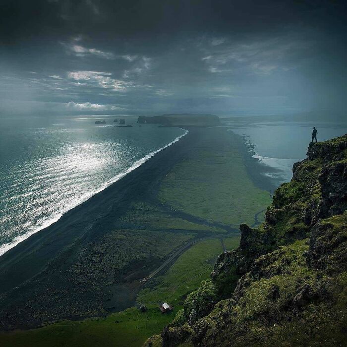 Person standing on cliff overlooking ocean and coastline, showcasing amazing pics of our world from a unique perspective