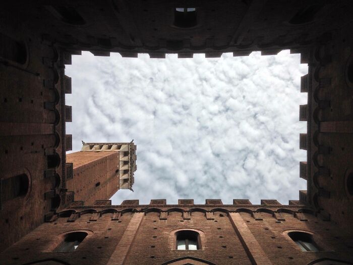 Looking up from inside a historic brick courtyard showing a tower and cloudy sky in amazing world perspective.
