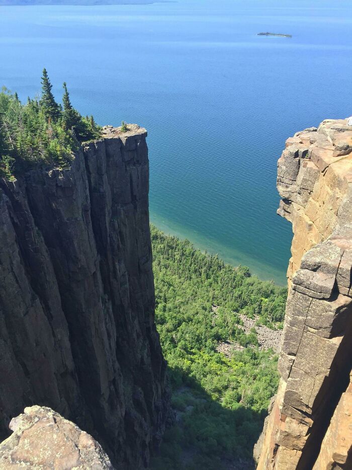 Cliff edge overlooking lush green forest and a calm blue lake, showing our world from an amazing different perspective.