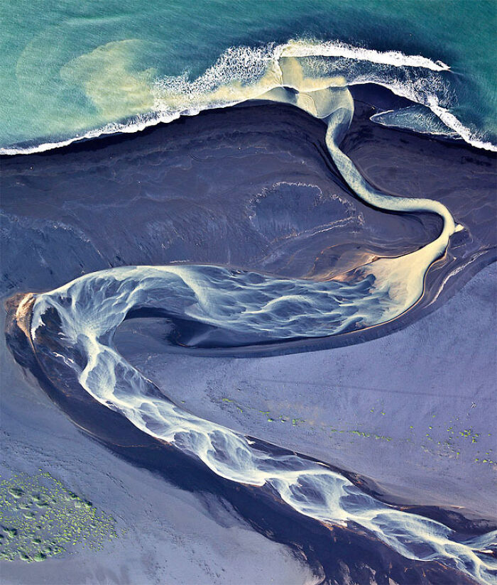 Aerial view of a winding river flowing through dark terrain showing our world from a completely different perspective.