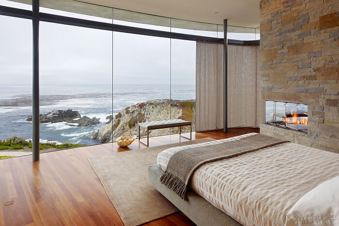 Modern bedroom with ocean view through floor-to-ceiling windows, showcasing an amazing perspective of nature and interior design.