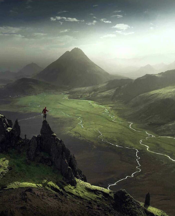 Person standing on rocky peak overlooking winding river and mountains in an amazing pic showing our world from a different perspective