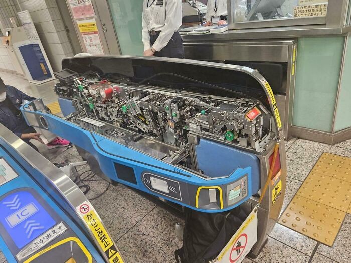 Complex inner mechanical components of a modern ticket gate system exposed for maintenance in a train station setting.