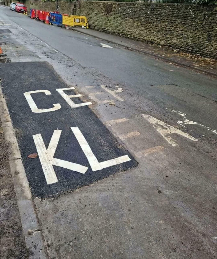 Faded road marking covered partially by fresh asphalt with poorly done repainting, showing people not even trying.