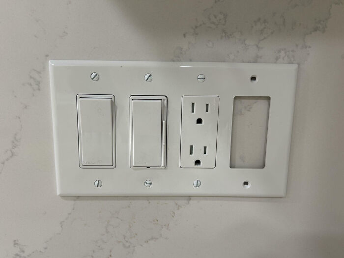 Electrical outlet and light switches installed with an empty space, showcasing a funny example of not my job appliance setup.