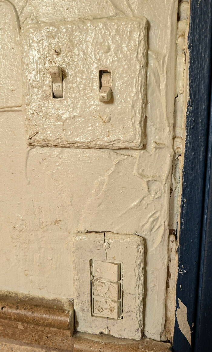 Light switches painted over with rough texture, showing a funny example of people not even trying to maintain proper electrical fixtures.