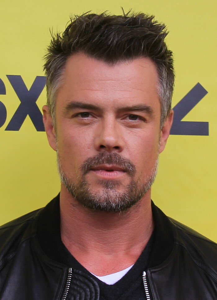 Josh Duhamel posing in a black jacket with a yellow background, showcasing a casual and confident look.