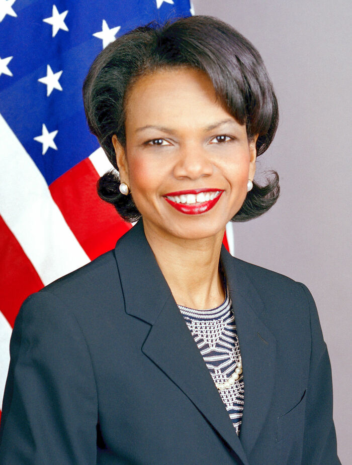 Condoleezza Rice smiling in formal attire with American flag background, highlighting bio and career highlights.