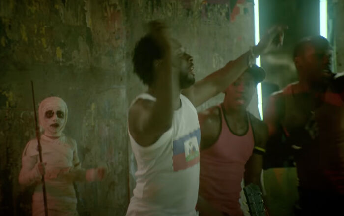 Child in spooky mummy costume photobombs group of men dancing energetically indoors, capturing an epic photobomb moment.