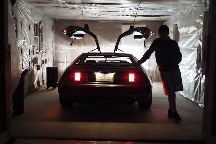 Person standing next to a DeLorean car with open gull-wing doors in a dimly lit garage, showcasing dream fulfillment.