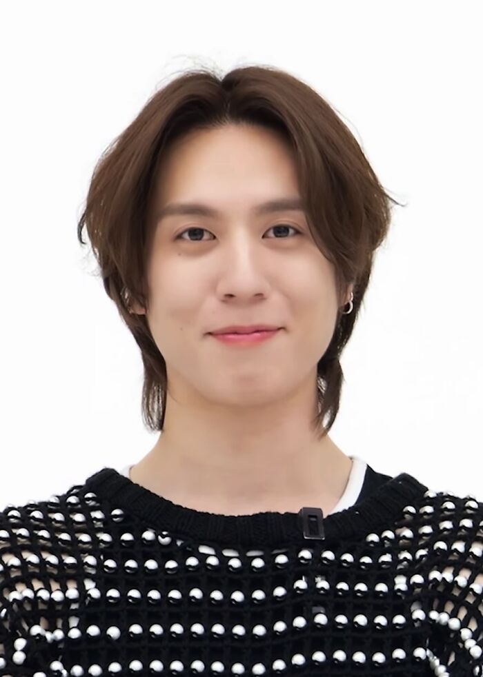 Yugyeom smiling with medium-length hair, wearing a black mesh sweater, posing against a white background.