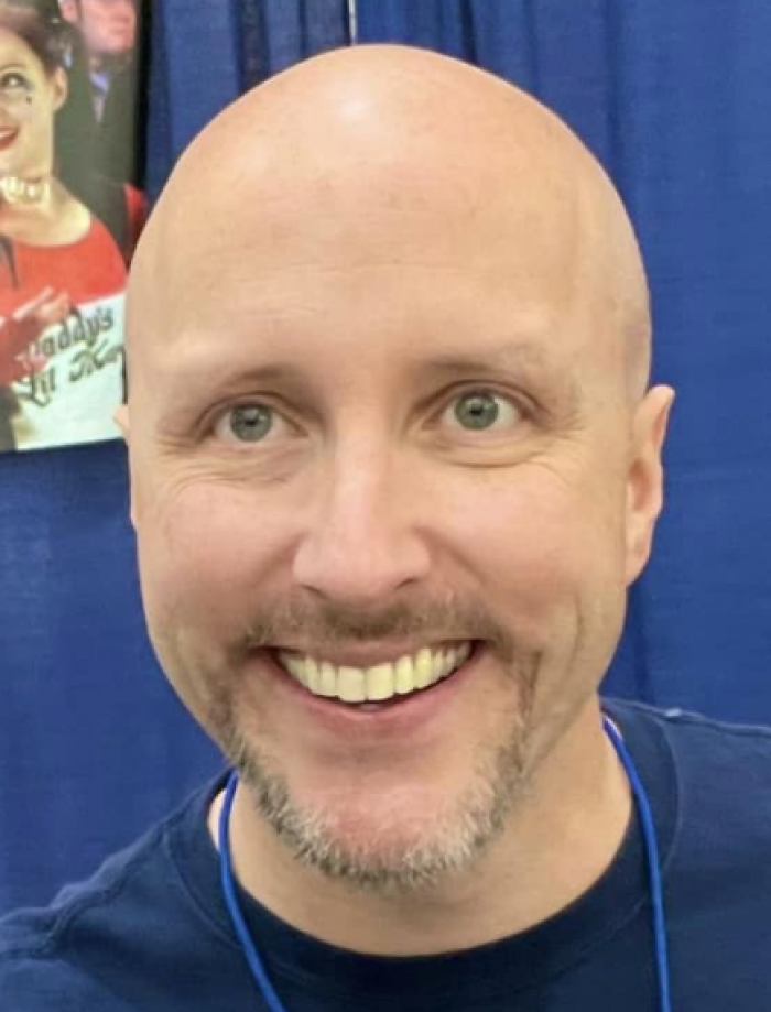 Doug Walker smiling at an event, with a blue backdrop and a casual dark shirt, highlighting his bio and career.