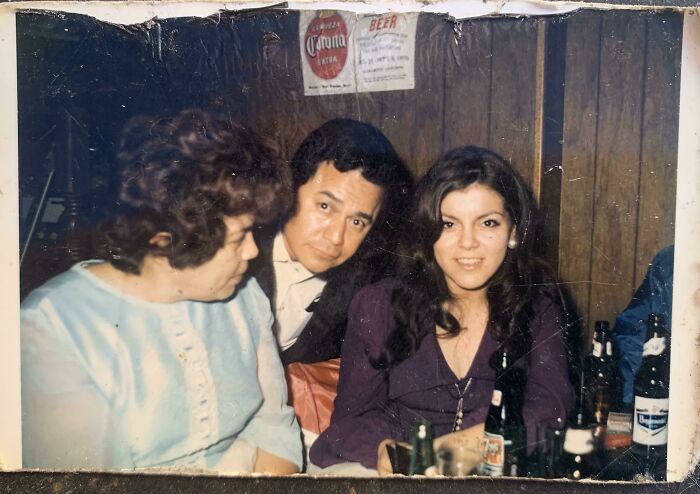 Three people sitting at a table with drinks, featuring a classic photobomb moment that made everyone laugh.