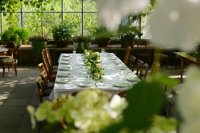 Wedding table set with white linens and floral centerpieces in a sunlit room, highlighting wedding and community event themes. Wedding table set with white linens and floral centerpieces in a sunlit room, highlighting wedding and community event themes.