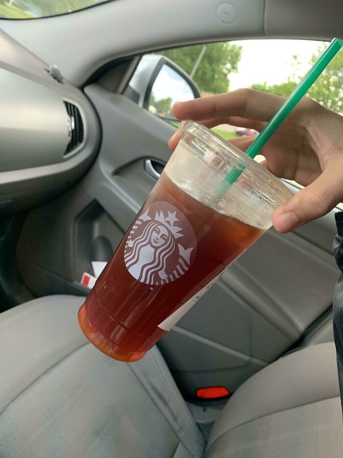 Hand holding a Starbucks iced drink inside a car, highlighting funny steak and lobster complaints about juiciness and butter.