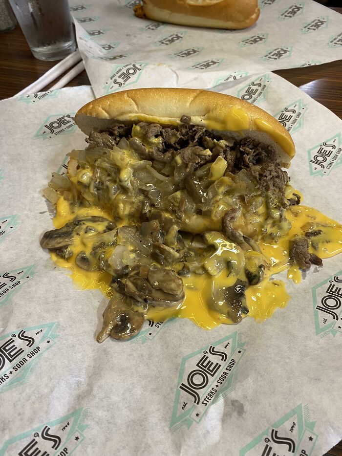 Philly cheesesteak sandwich with juicy steak, melted cheese, sautéed mushrooms, and onions on branded parchment paper.