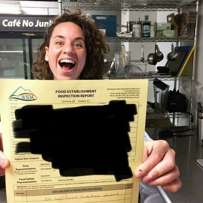 Woman excitedly holding a food establishment inspection report in a kitchen, celebrating turning her dream into reality.