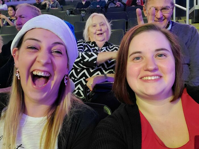 Two women smiling for a selfie with an elderly woman photobombing in the background, creating an epic photobomb moment.