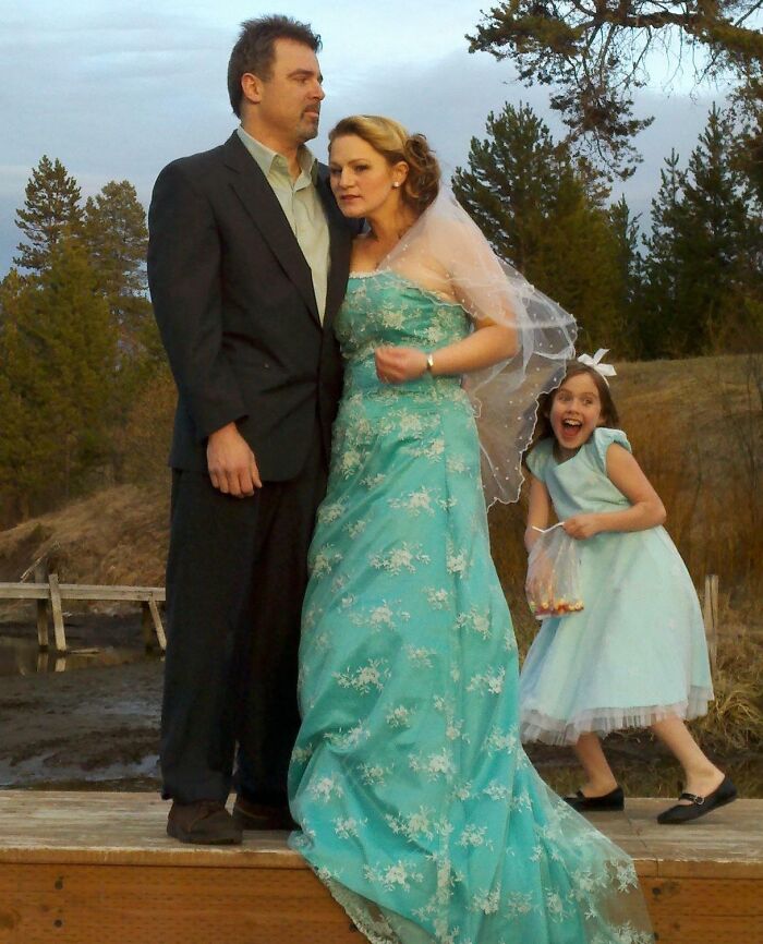 Couple dressed for formal photo with a young girl photobombing, capturing an epic photobomb moment outdoors.