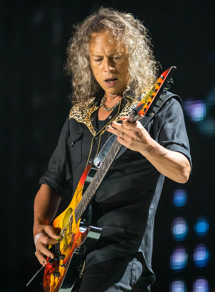 Kirk Hammett playing electric guitar on stage during a live performance, wearing a black shirt with leopard print details.