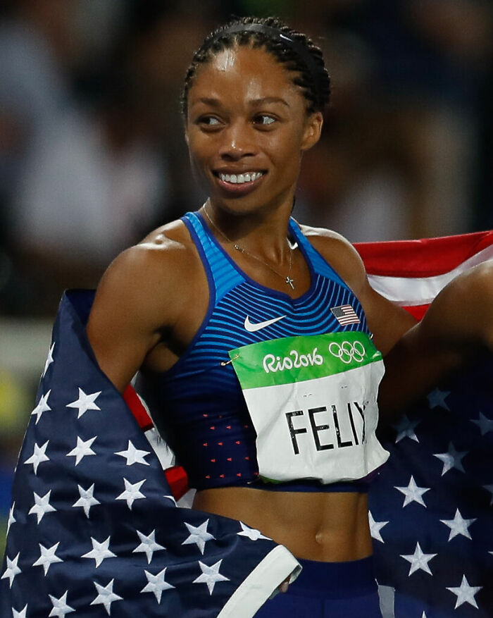 Allyson Felix celebrating with American flag at Rio 2016 Olympics after a track and field victory.