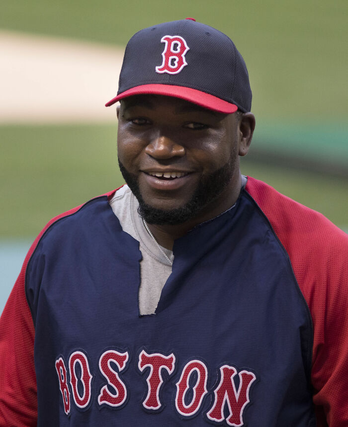David Ortiz smiling in Boston baseball gear during a practice session at the baseball field.