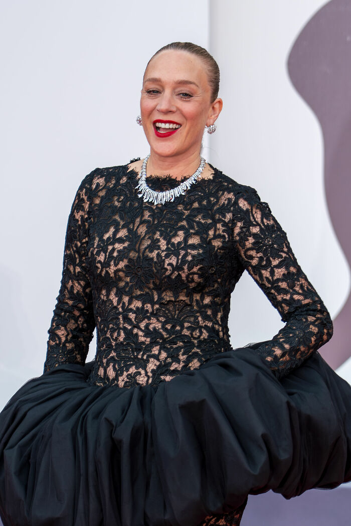 Chloë Sevigny in a black lace dress with bold red lipstick and diamond necklace at a formal event.