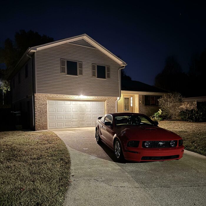 Red sports car parked in driveway of a suburban house at night, showcasing dreams turned into reality.