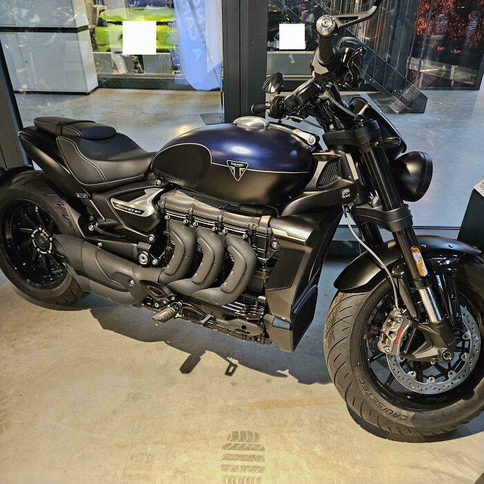 Black Triumph motorcycle parked indoors with matte finish and unique exhaust design, showcasing big and small dreams turned reality.
