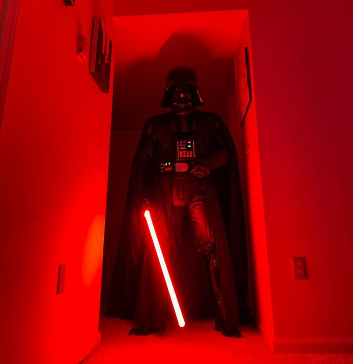 Person in detailed Darth Vader costume holding red lightsaber in a dimly lit hallway, showcasing dream cosplay brought to life.
