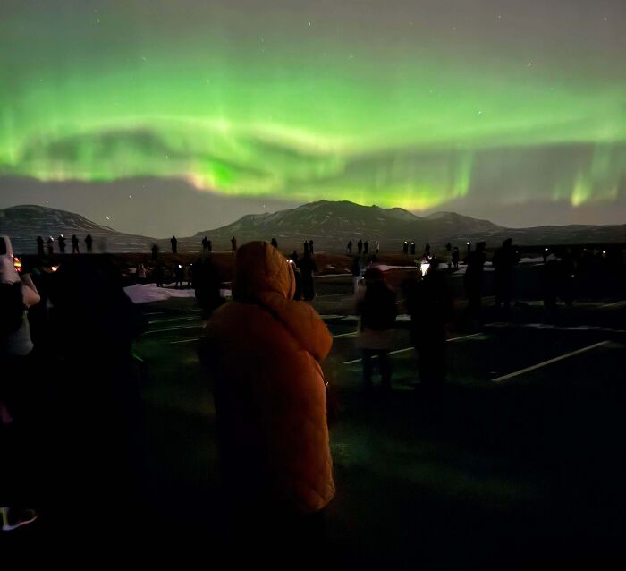 People inspired by dreams watching vivid green northern lights over snowy mountains on a clear night.