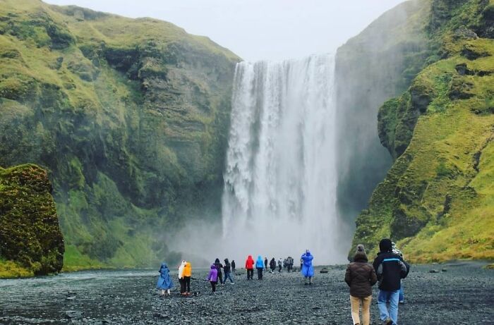 Tourists in colorful jackets walking toward a large waterfall, capturing moments of big and small dreams turned into reality.