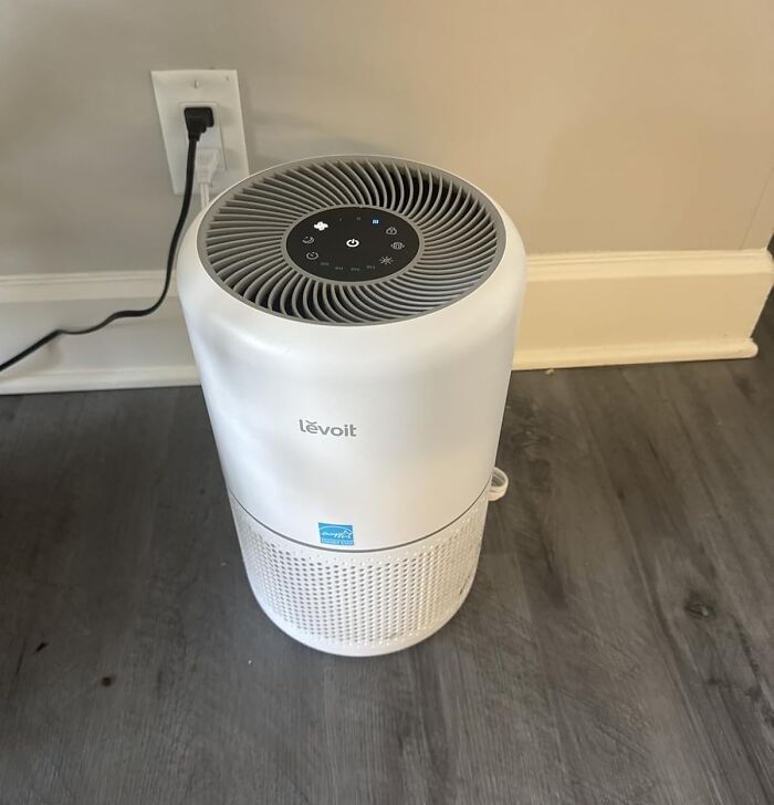 White Levoit air purifier plugged into wall outlet on hardwood floor with Black Friday Week hot deals concept.