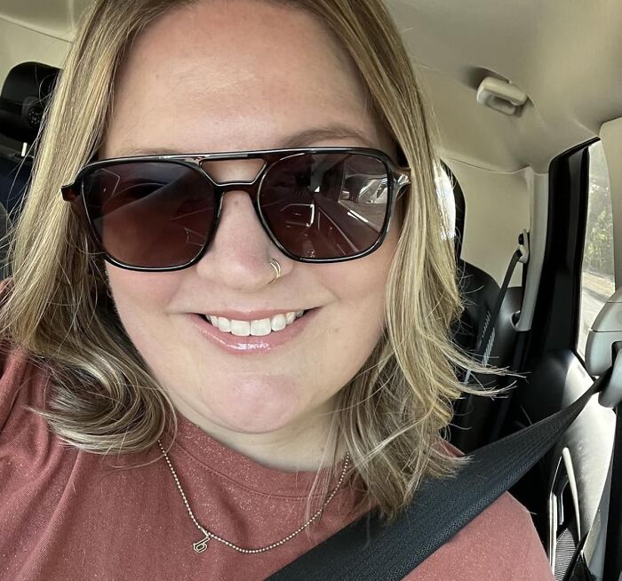 Smiling woman wearing sunglasses and a nose ring inside a car, enjoying Black Friday week deals and shopping vibe.