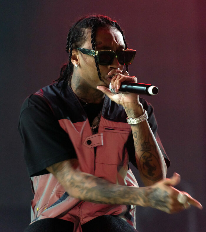 Tyga performing on stage wearing sunglasses and a pink vest, showcasing his music career and style.