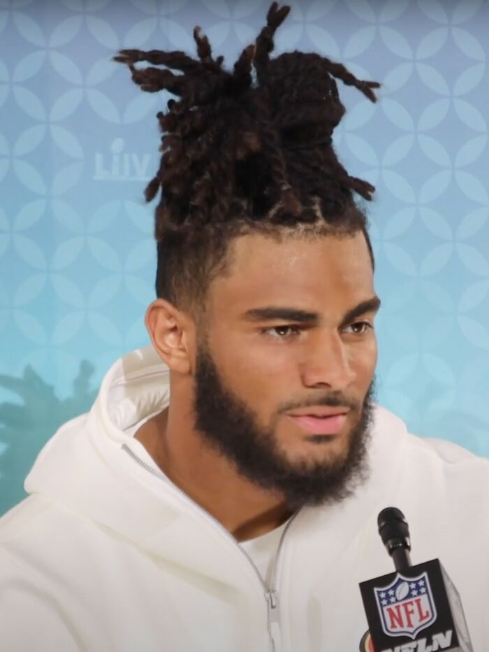 Fred Warner speaking at an NFL media event, wearing a white hoodie with a focused expression.
