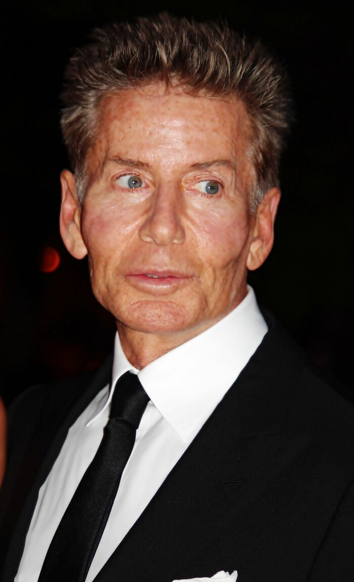 Calvin Klein wearing a black suit and tie at a formal event, showcasing his bio and career highlights.