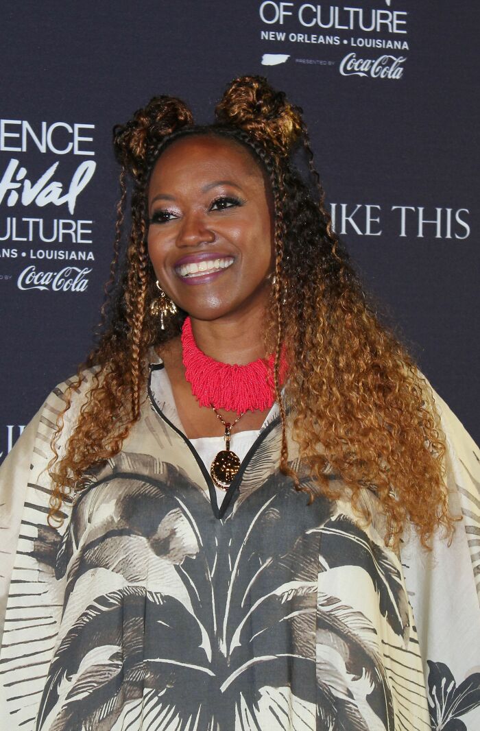 Erika Alexander smiling at an event, wearing a patterned outfit and a bold red necklace.