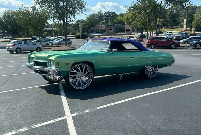 Green classic car with oversized rims and a purple soft top parked in a lot, showing stupidity on wheels modification.