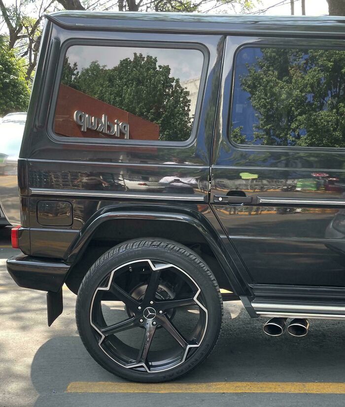 Black SUV with oversized car wheel rim and dual exhaust pipes, an example of failed attempts to make cars cooler on the road.
