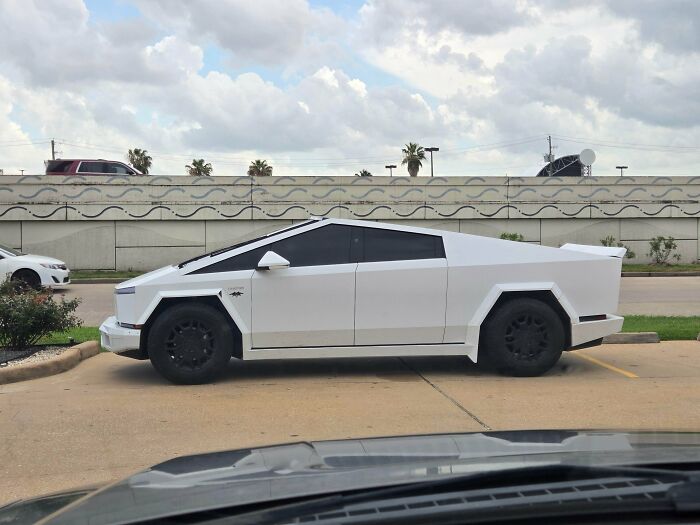 Futuristic white car with sharp angles and black wheels parked in a lot, showcasing a unique but questionable car modification.