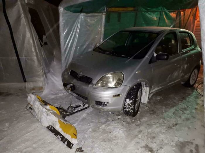 Silver compact car with a homemade snow plow attachment in a snowy garage, showcasing stupidity on wheels modification.