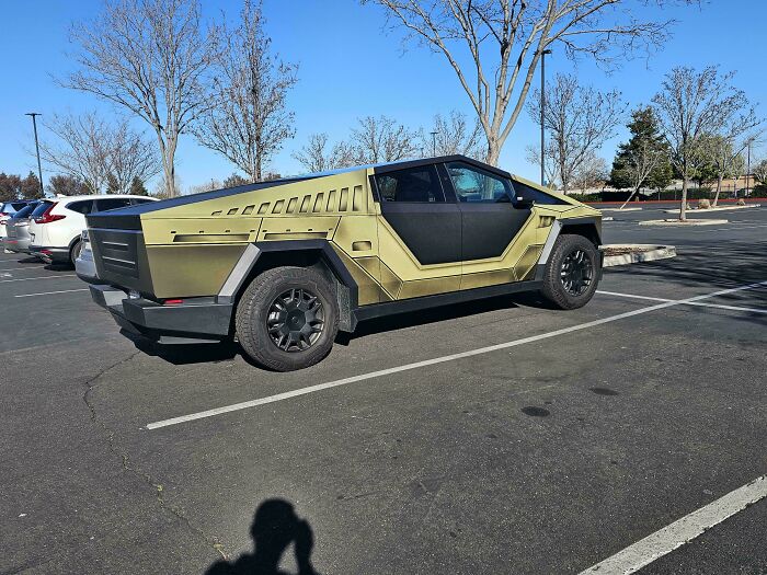 Angular custom truck painted in metallic olive green parked in an empty lot, showcasing a unique attempt at car customization.