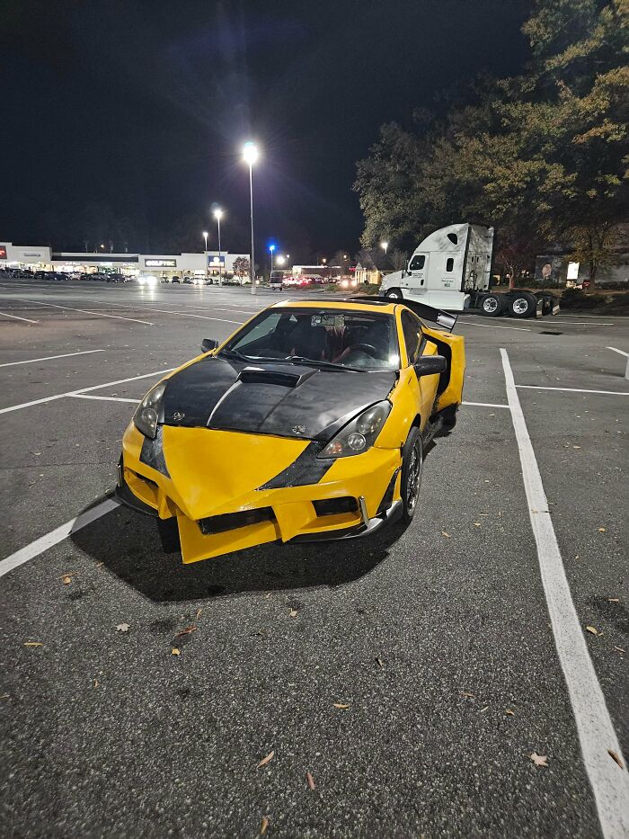 A poorly modified yellow and black car with a bulky, unusual front bumper parked in a lot, showing failed car customization.