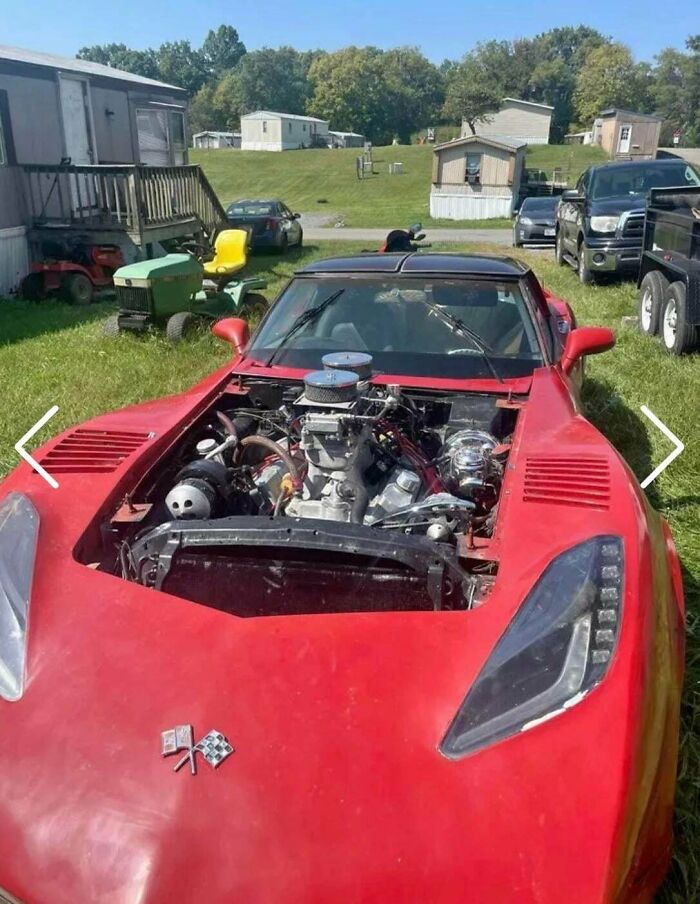 Red car with exposed engine in front of houses and vehicles, illustrating stupidity on wheels in car modification attempts.