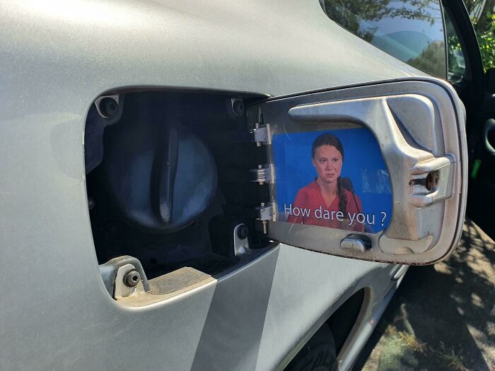 Car fuel cap with a hinge cover featuring a meme decal, showcasing creativity turned into stupidity on wheels.