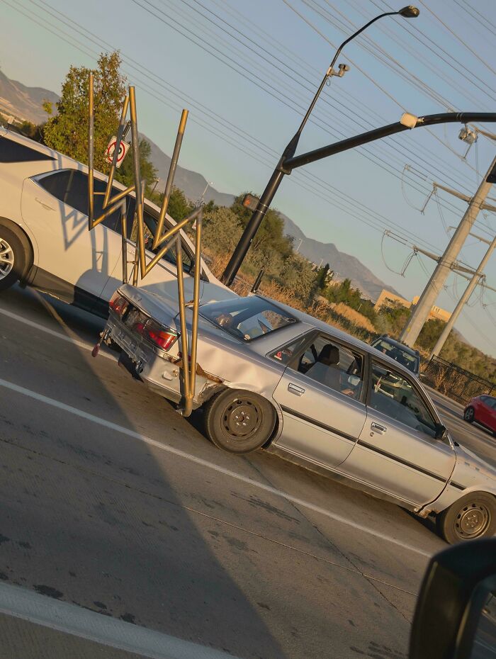 Silver sedan with large, unusual metal pipes attached to the back, a bizarre car modification fail on the road.